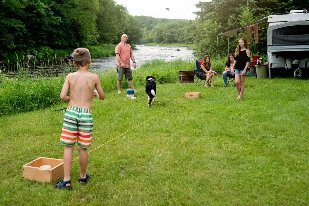 image of a family playing tossing game at campsite with lake in background