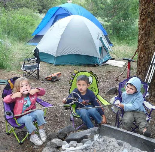 image of three kids sitting in camping chairs outside tent at campsite