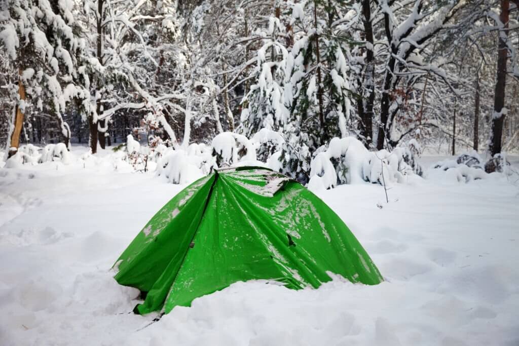 a green tent almost covered in snow