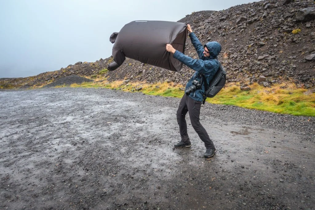 a man wearing a rain jacket holding a poncho in wind