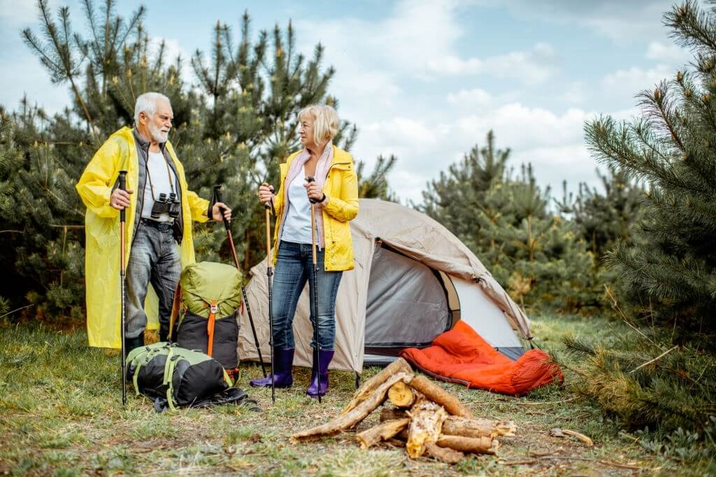 old couple holding trekking poles near a tent
