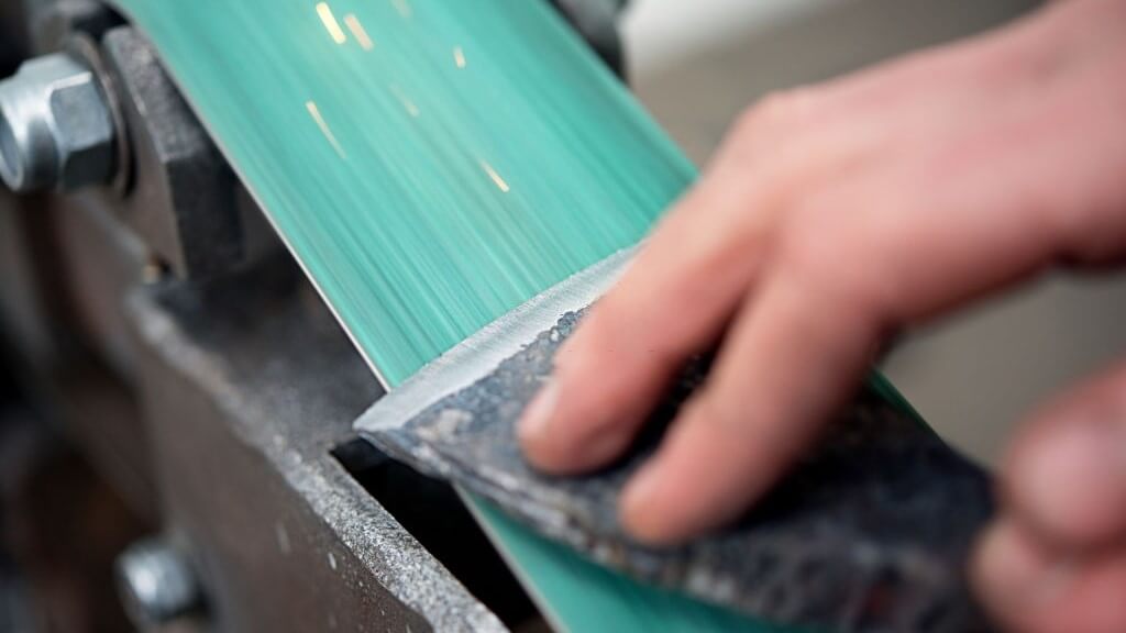 sharpening an old axe using a belt sander