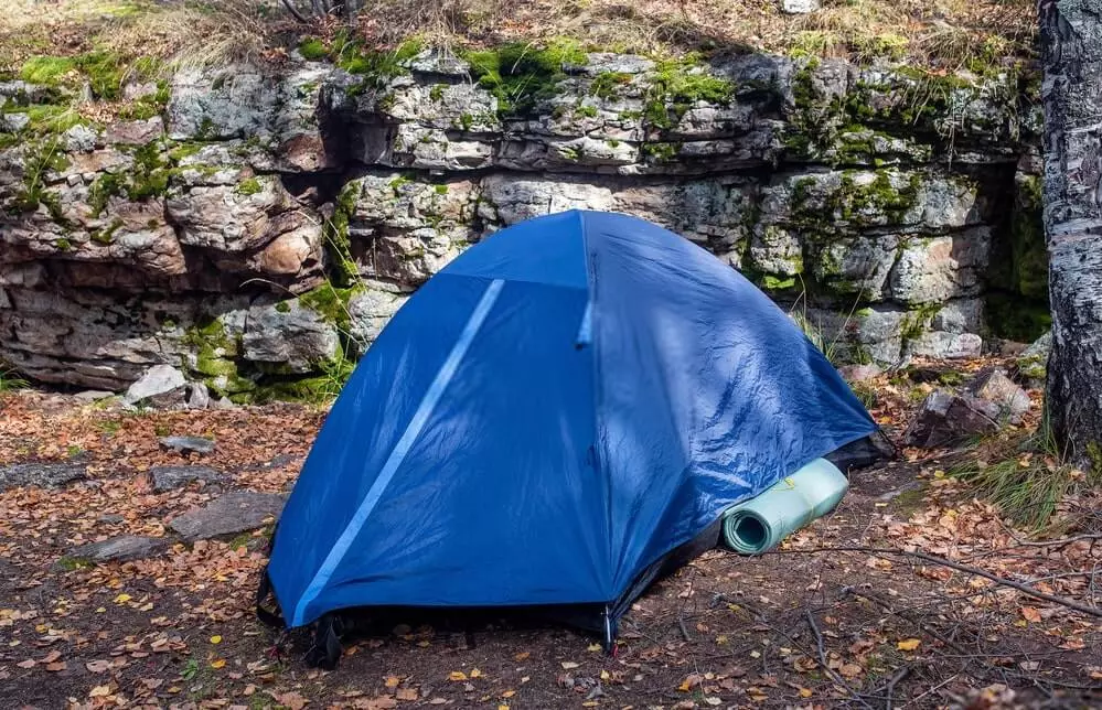 small blue camping tent set up near rocks