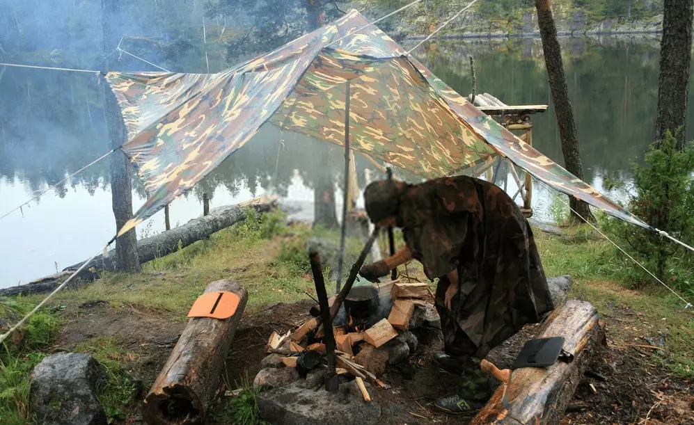 a camper sheltering against rain under a tarp