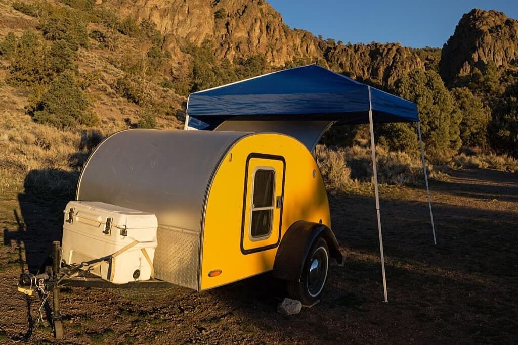 a yellow teardrop trailer packed under a canopy shade